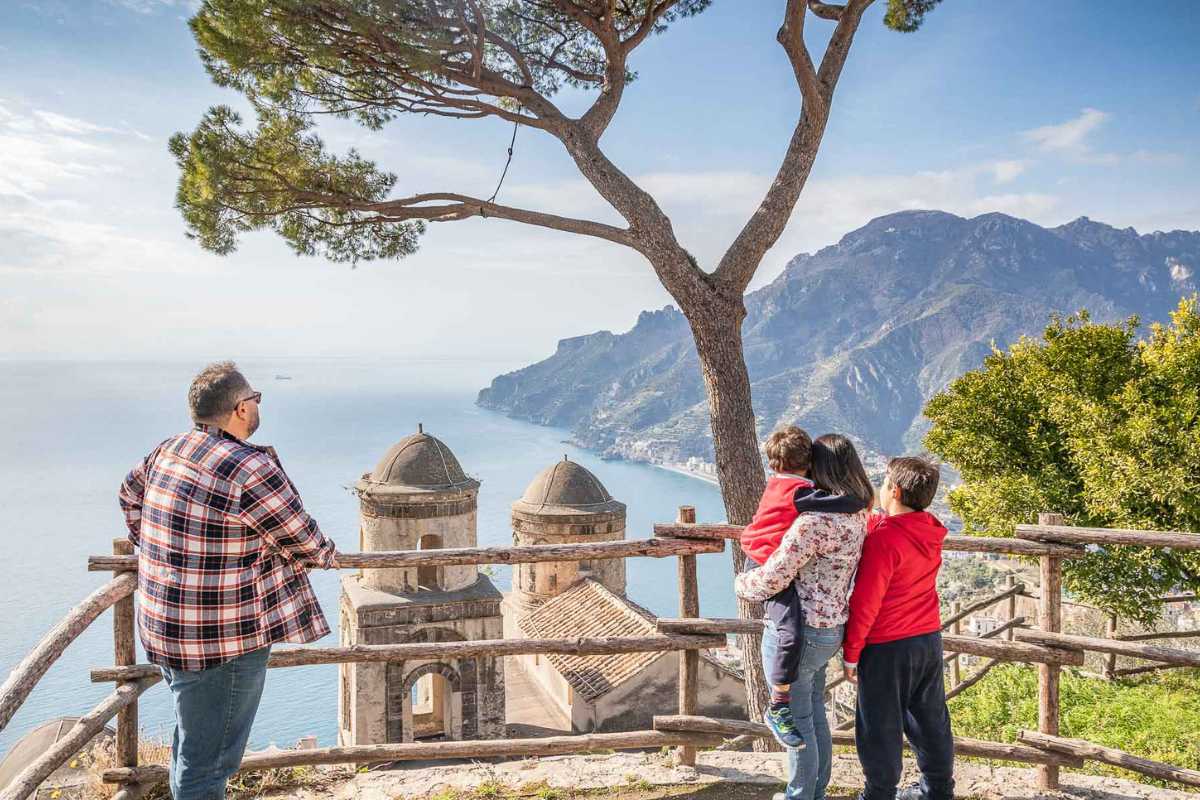 Bambini che giocano su un prato nel Parco Principessa di Piemonte, con vista sulla Costiera Amalfitana e Ravello in lontananza, atmosfera familiare e rilassata